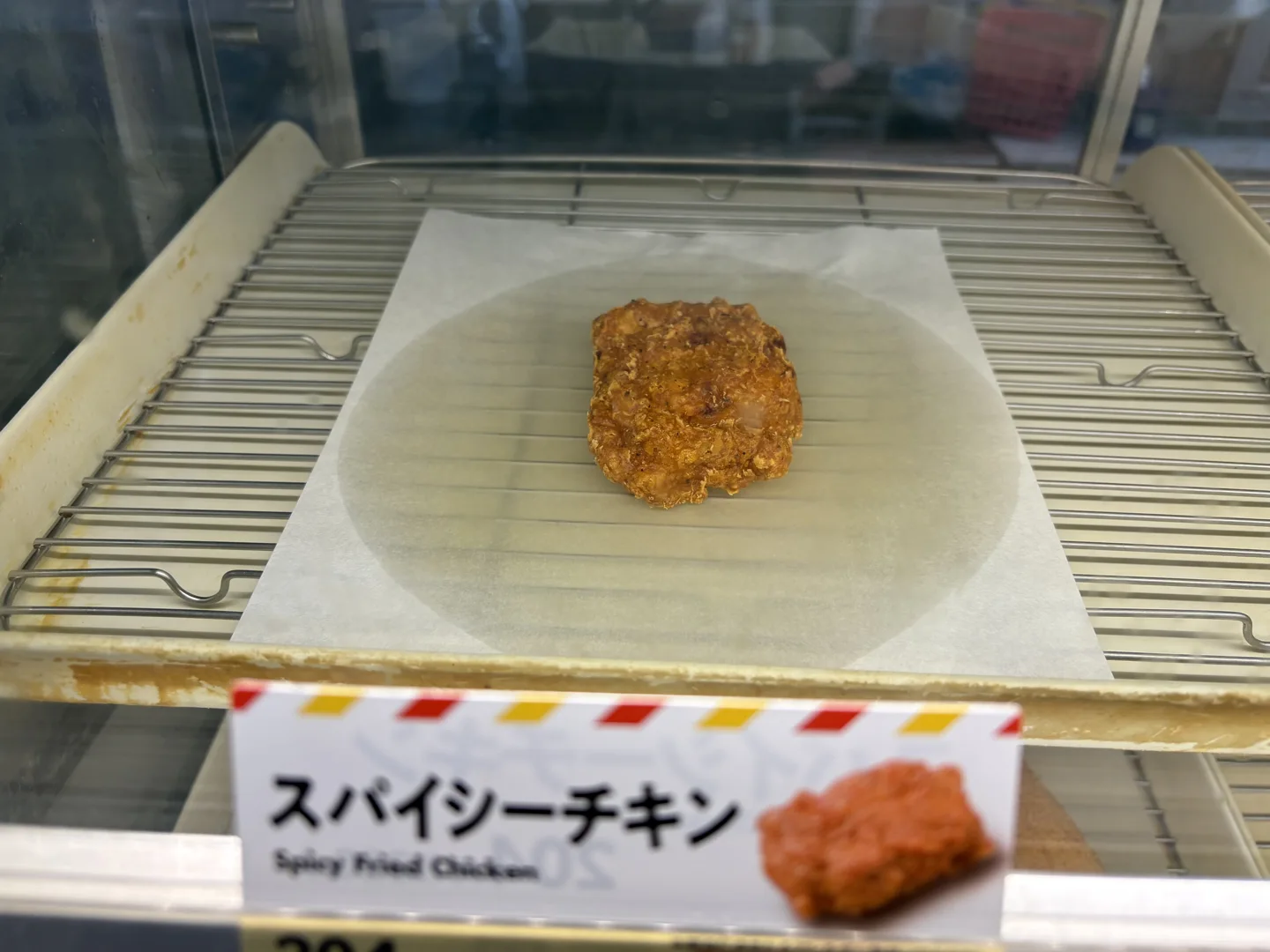 A piece of Spicy Chicken in a heated case with its separate product sign